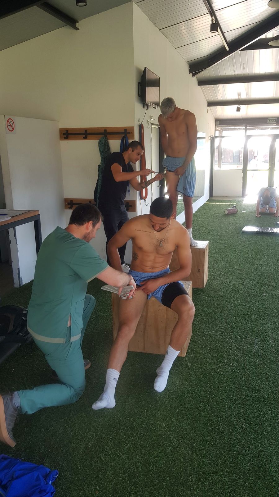 Juan Pablo Santroni mide un pliegue con un plicómetro a un deportista sentado en un cajón, mientras otro nutricionista mide a un segundo deportista