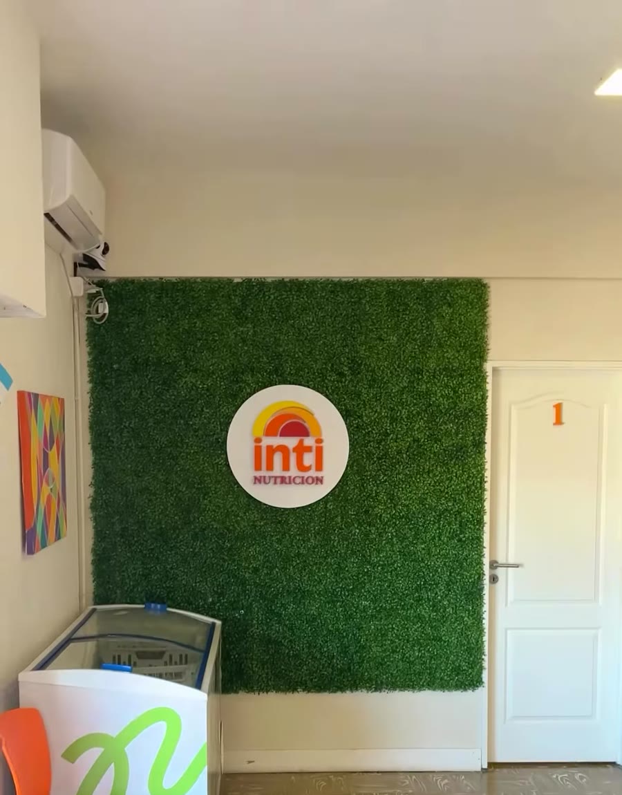 La recepción de Inti en el segundo piso: jardín vertical con el logo, la puerta del consultorio 2 y el estante de suplementos